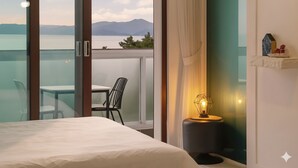 Hotelkamer met balkon, uitzicht op een meer en bergen, een bed, een tafel met stoelen en een lamp.