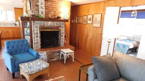 Uma sala de estar aconchegante com lareira, poltrona azul, sofá cinza e uma pequena mesa.