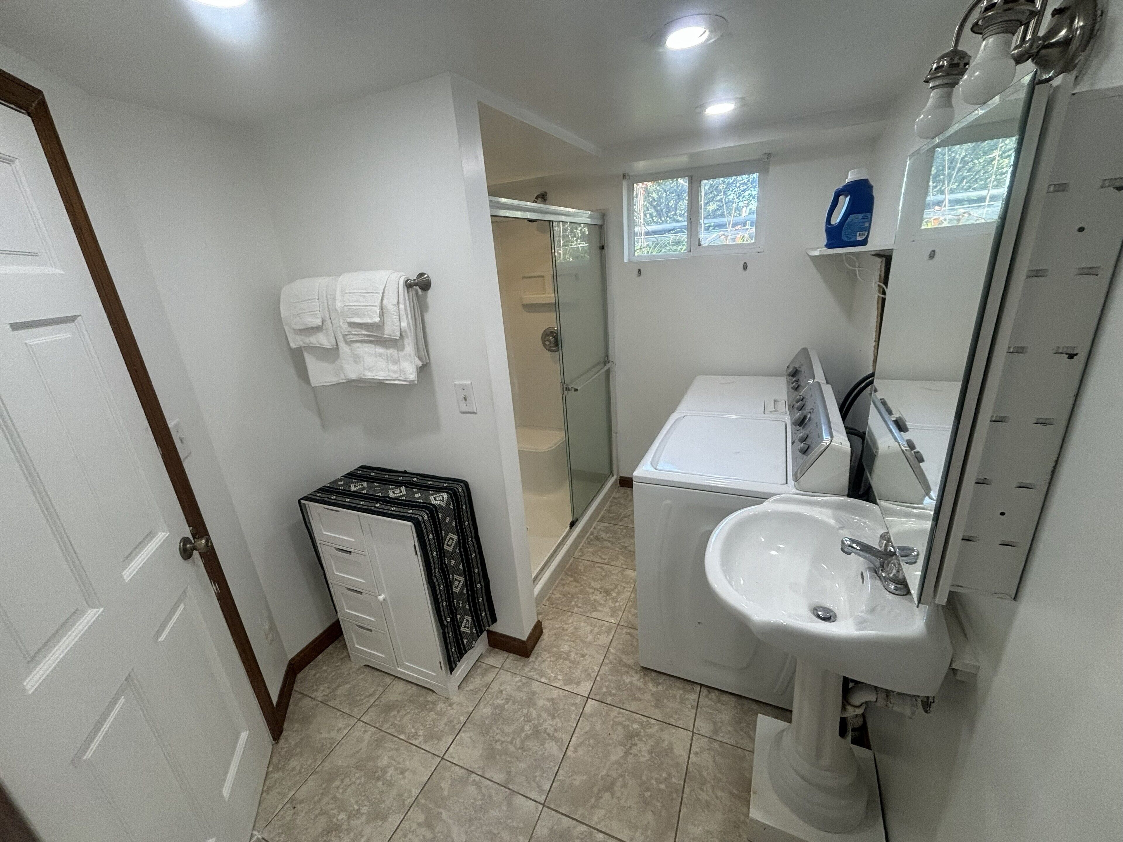 A bathroom with a white sink, a mirror, a glass shower enclosure, and a stack of black and white towels.