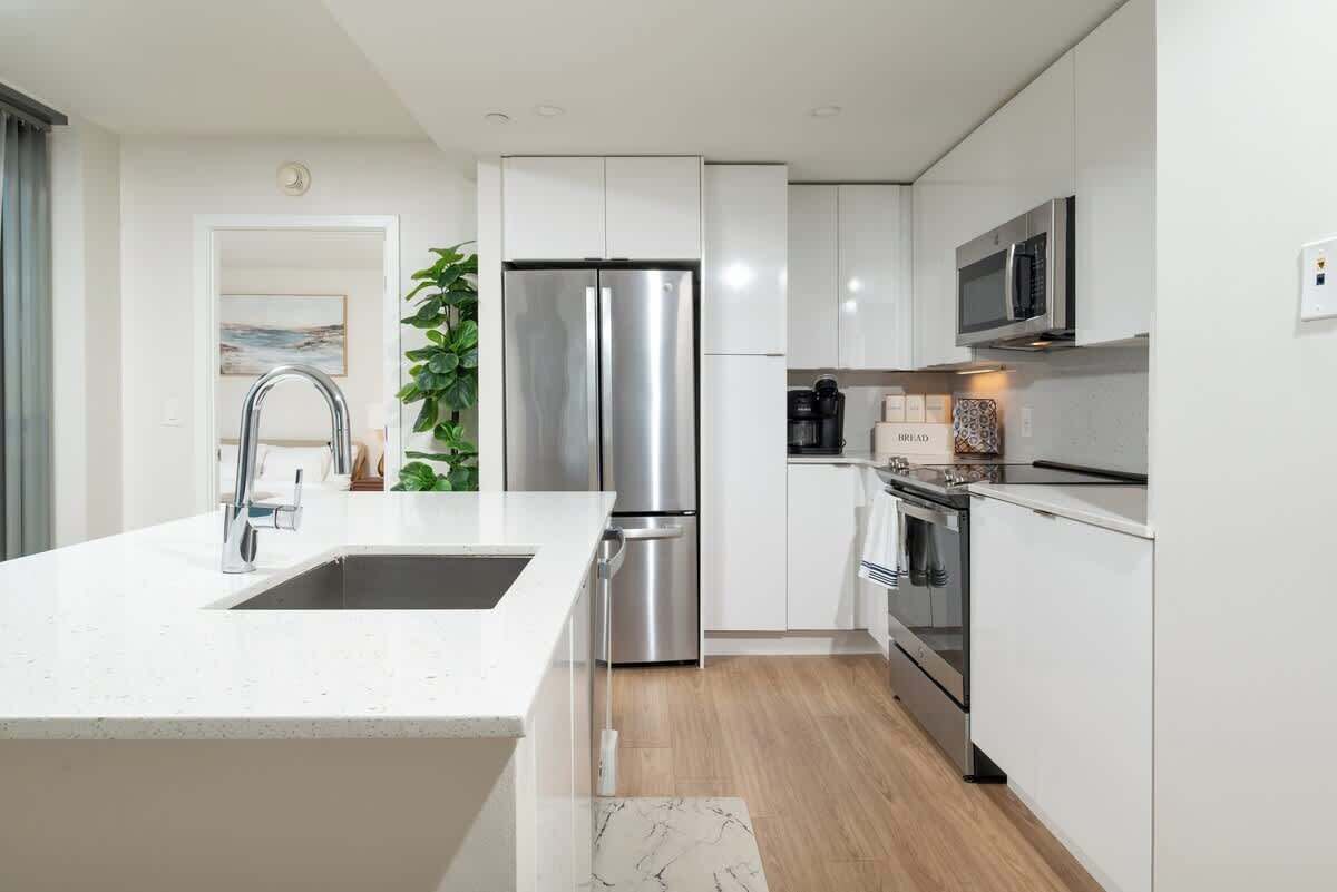 A modern kitchen with white cabinetry, stainless steel appliances, and a marble backsplash.
