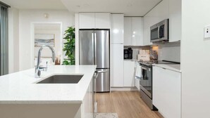 A modern kitchen with white cabinetry, stainless steel appliances, and a marble backsplash. - Central 2BR Condo in Downtown Boston & T-Station (Boston)