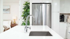 A modern kitchen with a stainless steel refrigerator, a white countertop, and a sink with a modern faucet. - Central 2BR Condo in Downtown Boston & T-Station (Boston)
