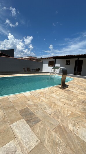 A swimming pool with a water feature, tiled flooring, and outdoor furniture. - House with a Pool in Caraguatatuba (Caraguatatuba)