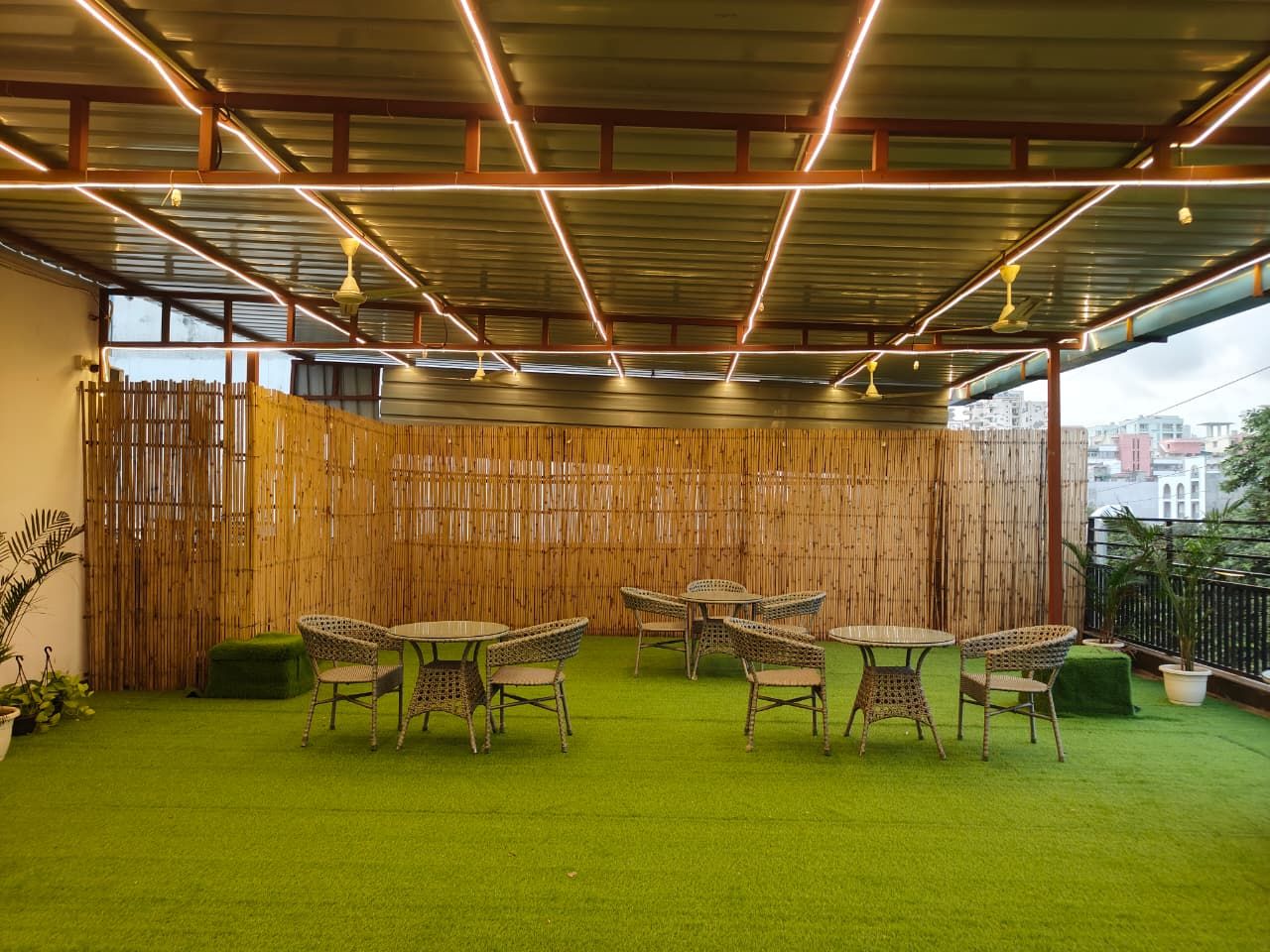 An outdoor patio with a bamboo fence, green artificial grass, wicker furniture, and hanging lights.