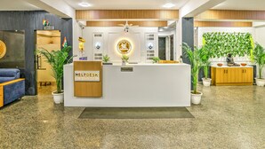 Un mostrador de recepción con un letrero que dice "HELPDESK I AM HERE TO HELP YOU", un área de recepción y una estatua de una figura sentada.