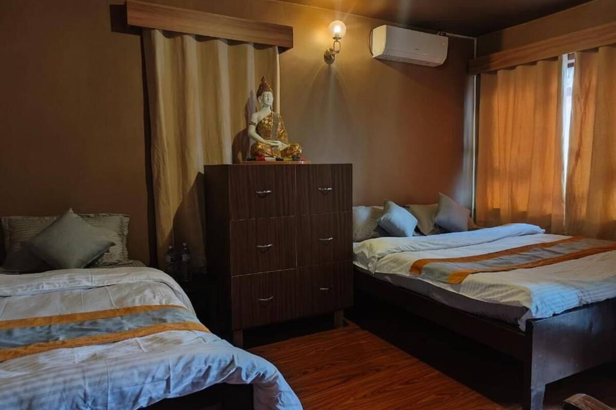 Ein Hotelzimmer mit zwei Betten, einem Kleiderschrank, einer Buddha-Statue und einer Wand-Klimaanlage.
