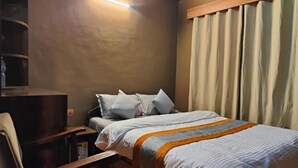 Ein Schlafzimmer mit einem Bett, einem Nachttisch, einem Sessel, einem Holzschrank und einem Fenster mit Vorhängen.