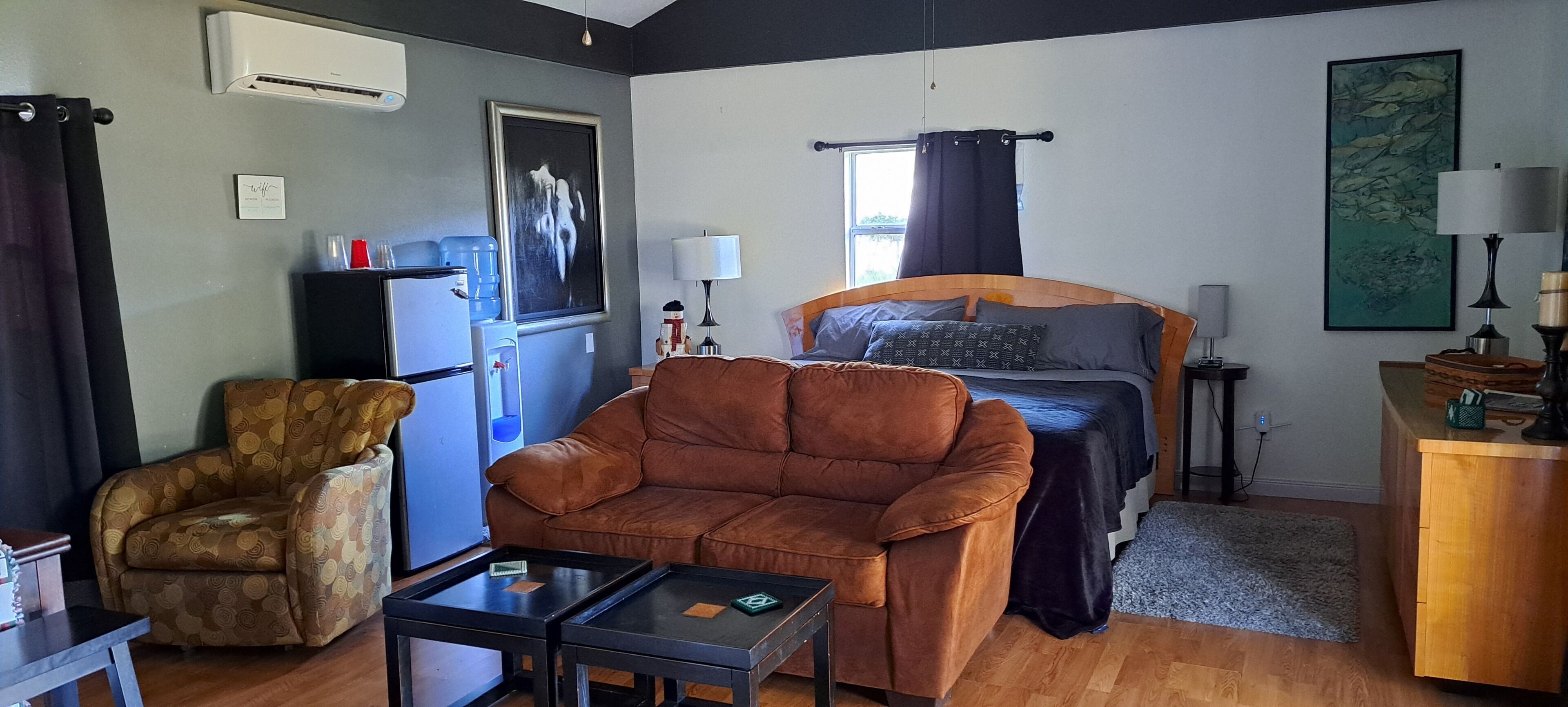 A compact room with a bed, a sofa, a chair, a small table, a desk, and a window with curtains.