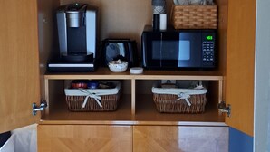 A wooden cabinet with a microwave, coffee maker, and baskets.