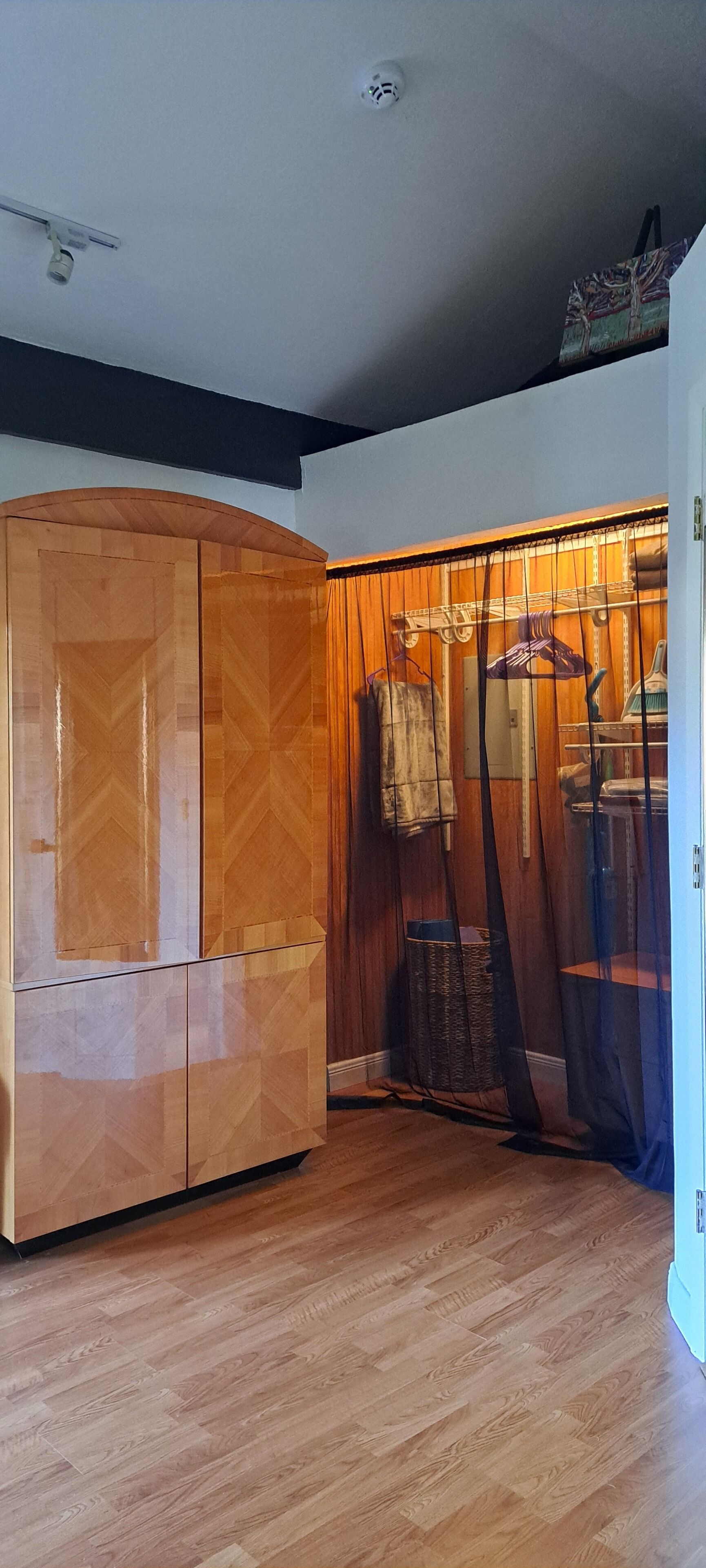 A room with a wooden wardrobe, a hanging rack with clothes, and a wooden floor.