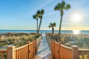 A wooden boardwalk leading to a beach with palm trees and a clear sky. - Beachfront Bliss! 1BR/2BA Sleeps 4 (Panama City Beach)