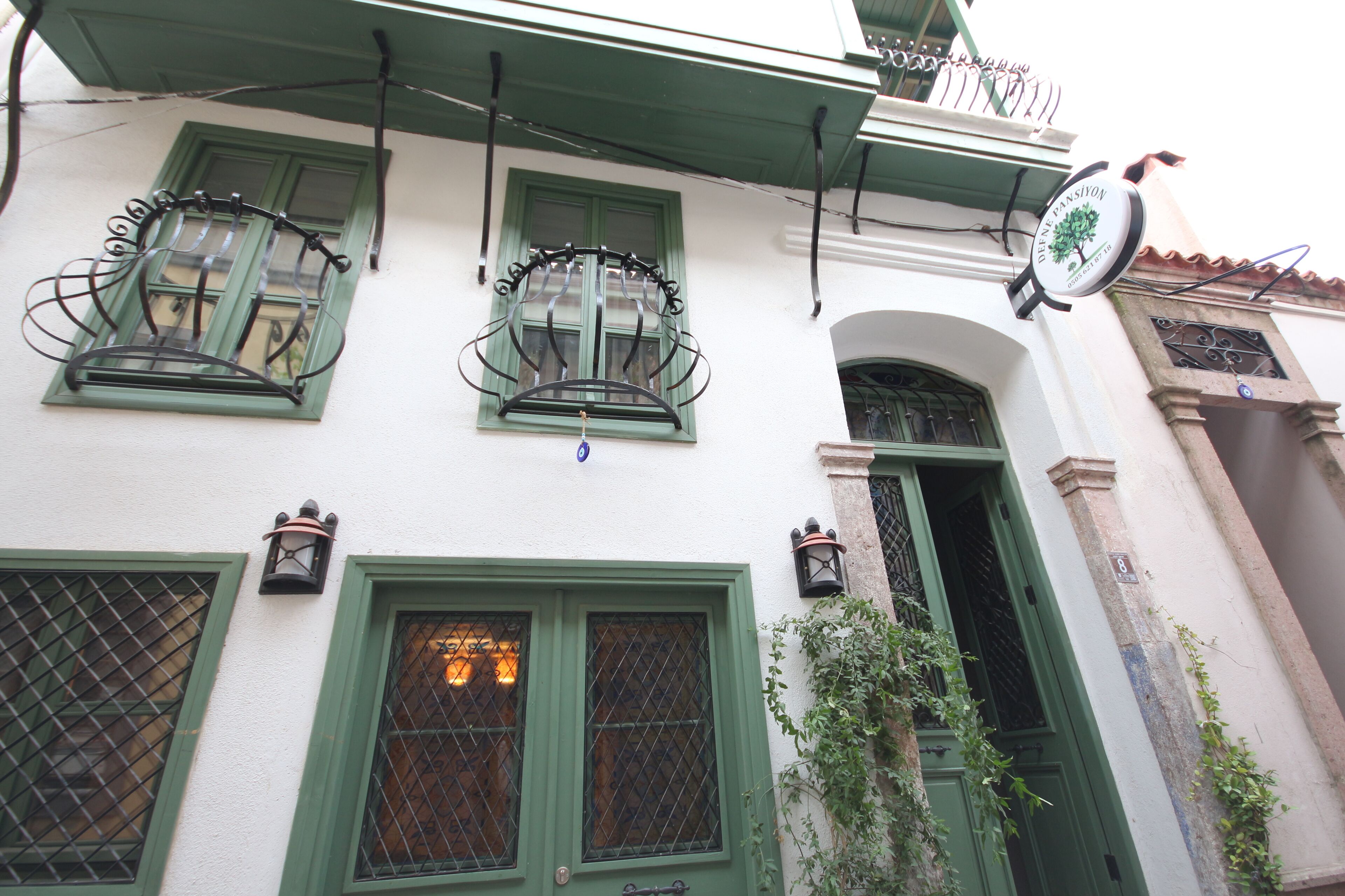 A building with green-framed windows, a balcony with a wrought iron railing, and a sign indicating a restaurant.