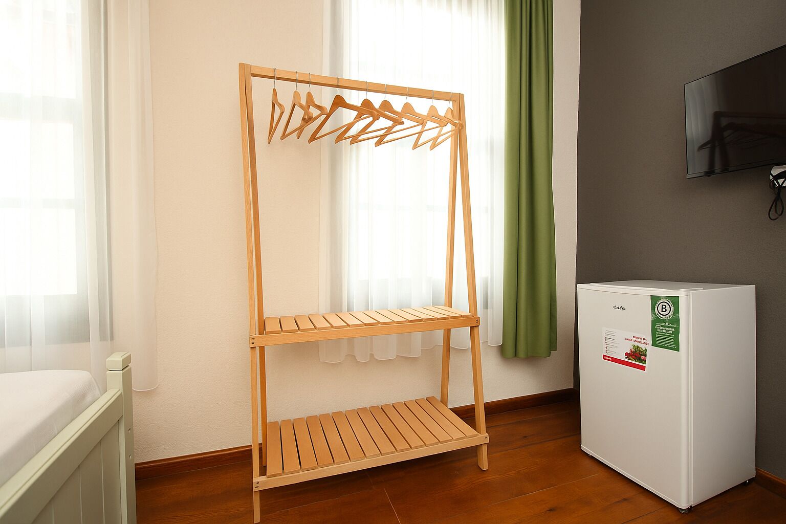 Quarto com um varal de madeira, um radiador branco e uma televisão na parede.