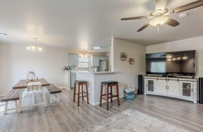 A modern kitchen with a central island, bar stools, a dining table, and a ceiling fan. - Cozy Modern 3-bedroom House in Gold Canyon Dark Sky Community & Mountain Views (Gold Canyon)