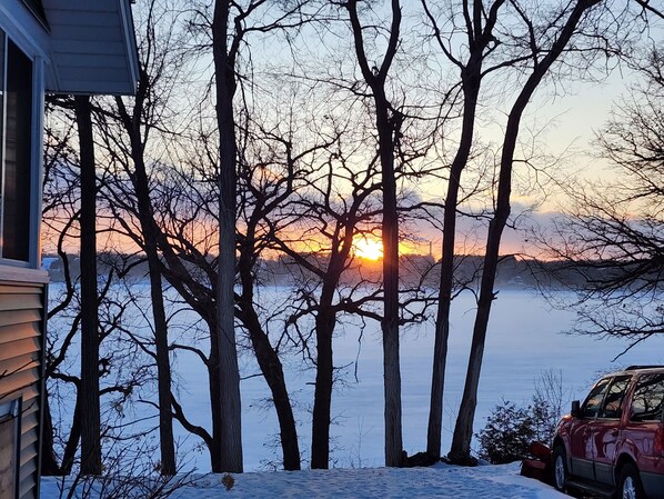 A house with a view of a sunset over a body of water, surrounded by trees.