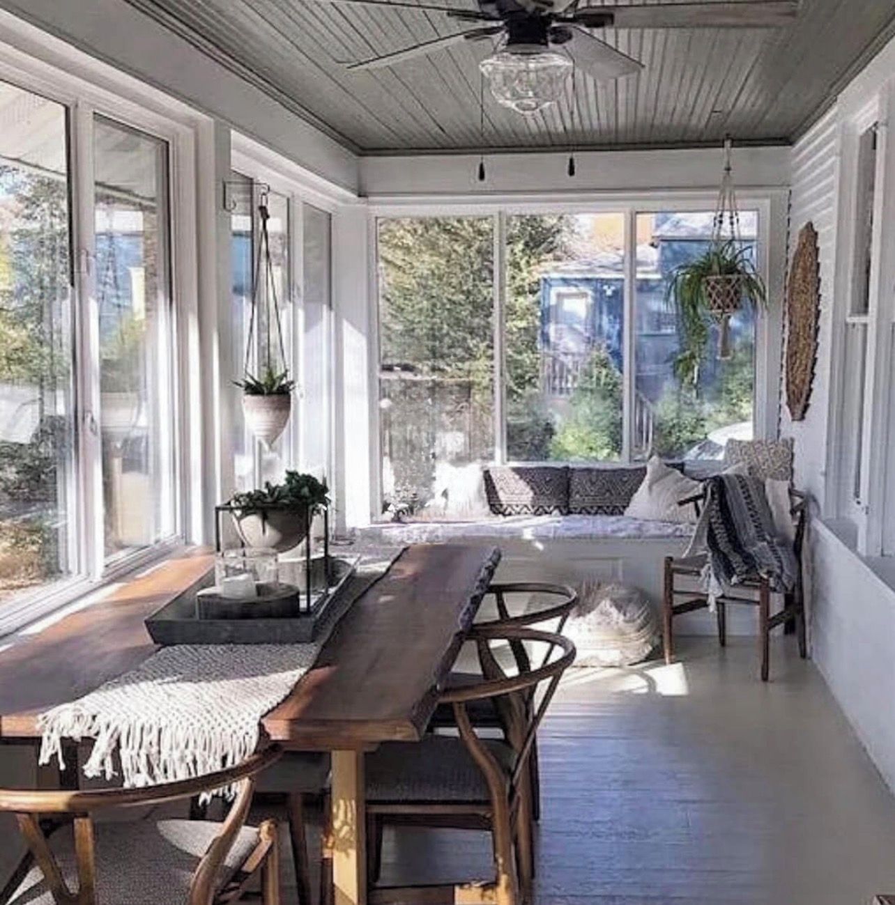 A sunroom with a wooden table and chairs, large windows, and a ceiling fan.