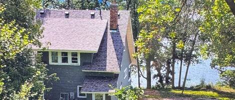 A two-story house with a stone chimney, a front porch, and a view of a lake.