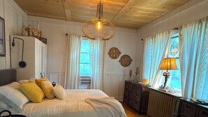 A bedroom with a bed, wooden floor, ceiling fan, window with curtains, dresser, and lamp.