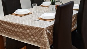 A dining area with a table set for four, surrounded by chairs, with a clock on the wall and shelves above holding various items. - Paramount Nest (Swindon)