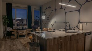 Une cuisine moderne dotée d’un grand îlot central, de meubles en bois et offrant une vue sur la ville au crépuscule.