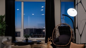 Un salon moderne avec un fauteuil suspendu, une table à manger avec des chaises et une grande fenêtre donnant sur la ville.