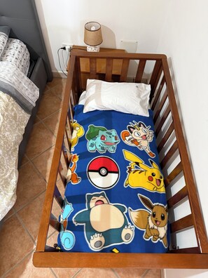 Pieni puinen sänky, jossa on sininen Pokémon-aiheinen päiväpeite ja valkoinen tyyny.