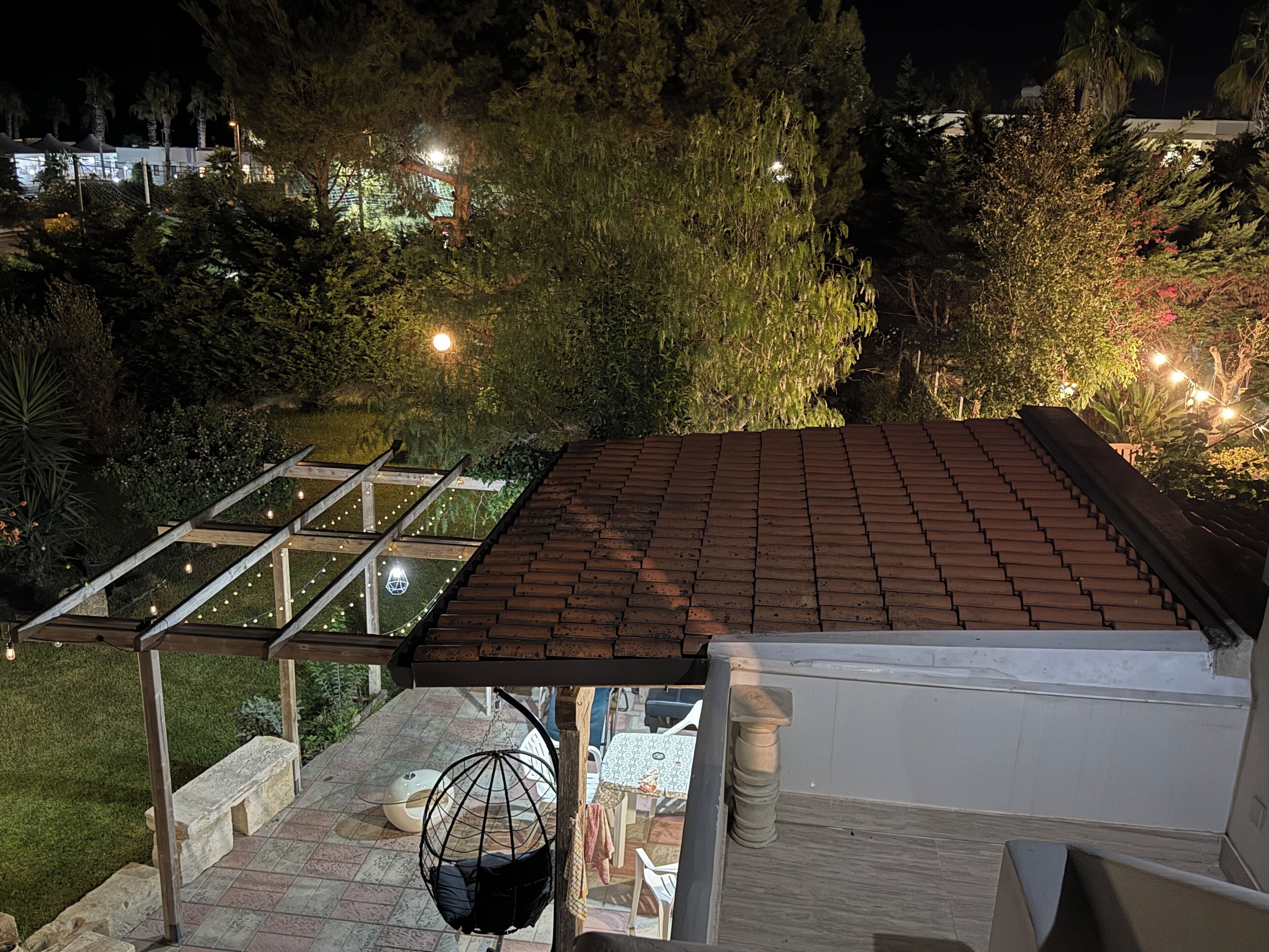 Een terras op het dak met pannendak, een pergola met lichtslingers en een hangstoel.