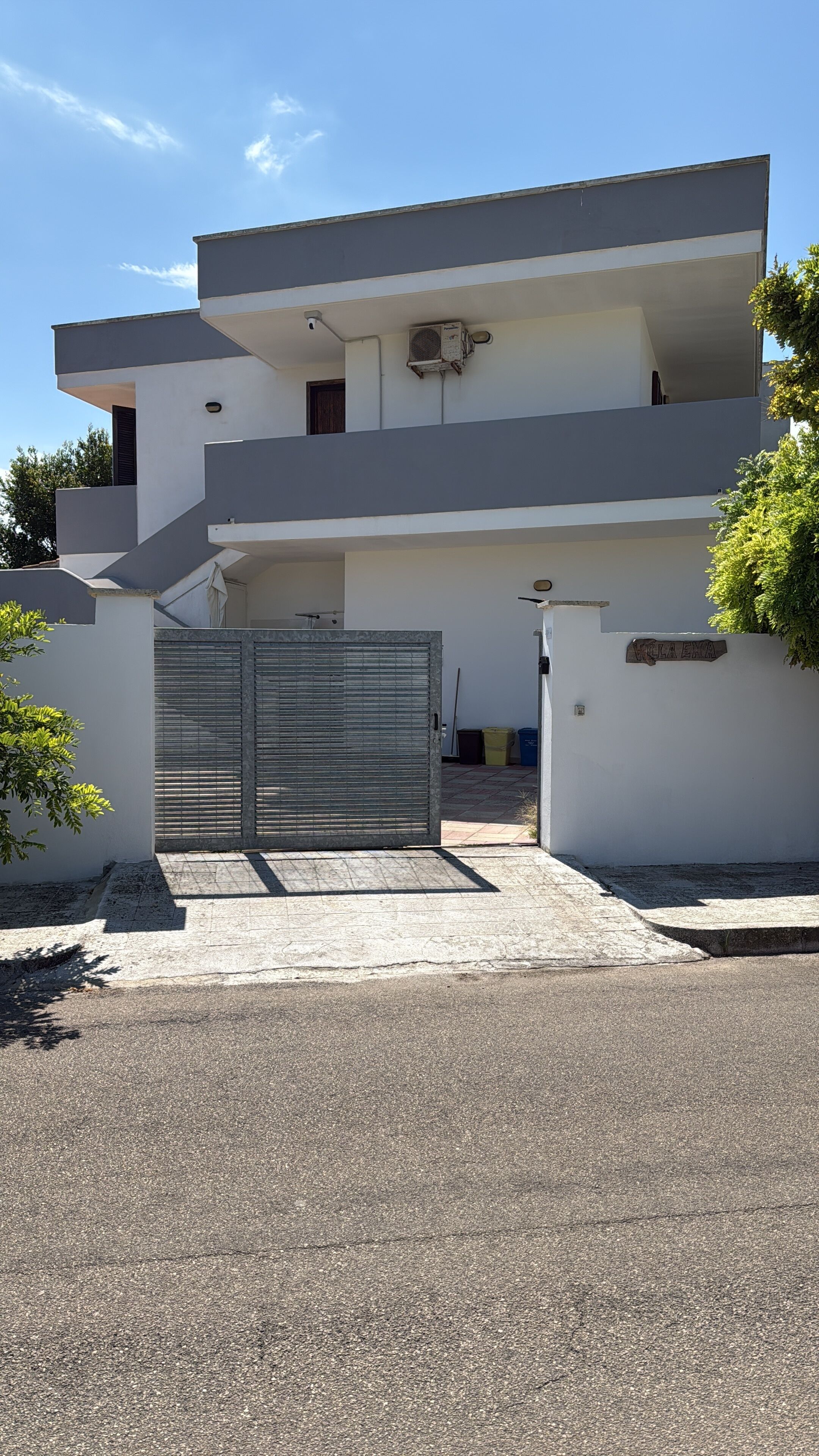 Un bâtiment moderne à deux étages, doté d’une entrée sécurisée par un portail, d’un toit plat et d’un appareil de climatisation visible.