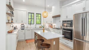 A modern kitchen with white cabinets, a stainless steel refrigerator, and a central island with stools. - Tower on the Tuck: Entire home on the Tuckaseegee River near WCU -Riverfront (Cullowhee)