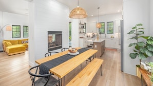 A modern kitchen with white cabinetry, a central island, and a dining area with wooden tables and benches. - Tower on the Tuck: Entire home on the Tuckaseegee River near WCU -Riverfront (Cullowhee)
