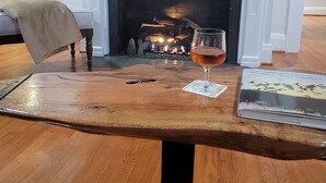 A wooden coffee table with a glass of wine and a book, a fireplace, and a TV mounted above it. - Reconnect with Nature Farmhouse sleeps 6, two large bathrooms, full kitchen, (Whiteville)