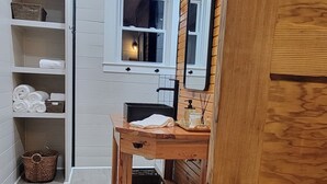 A wooden door with a metal handle, a wooden table with a mirror, and a shelf with towels and baskets. - Reconnect with Nature Farmhouse sleeps 6, two large bathrooms, full kitchen, (Whiteville)