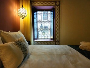 A hotel room with a bed, a decorative window with intricate metalwork, and a hanging light fixture. - Riad Dar Mazaj Fes (Fes)