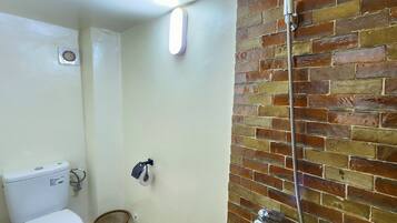 A bathroom with a toilet, a shower, and a brick wall.