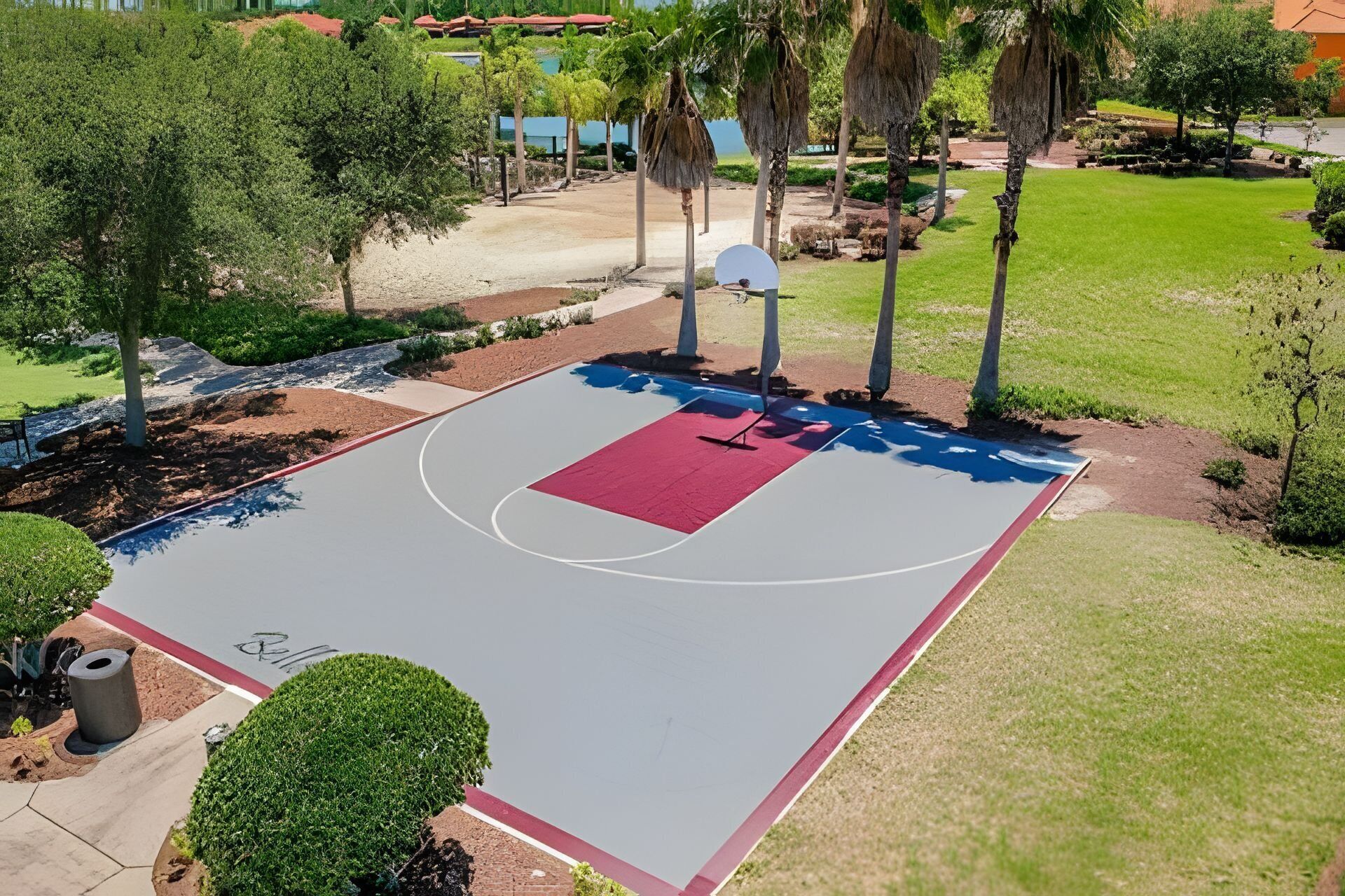 An outdoor basketball court surrounded by trees and a grassy area.