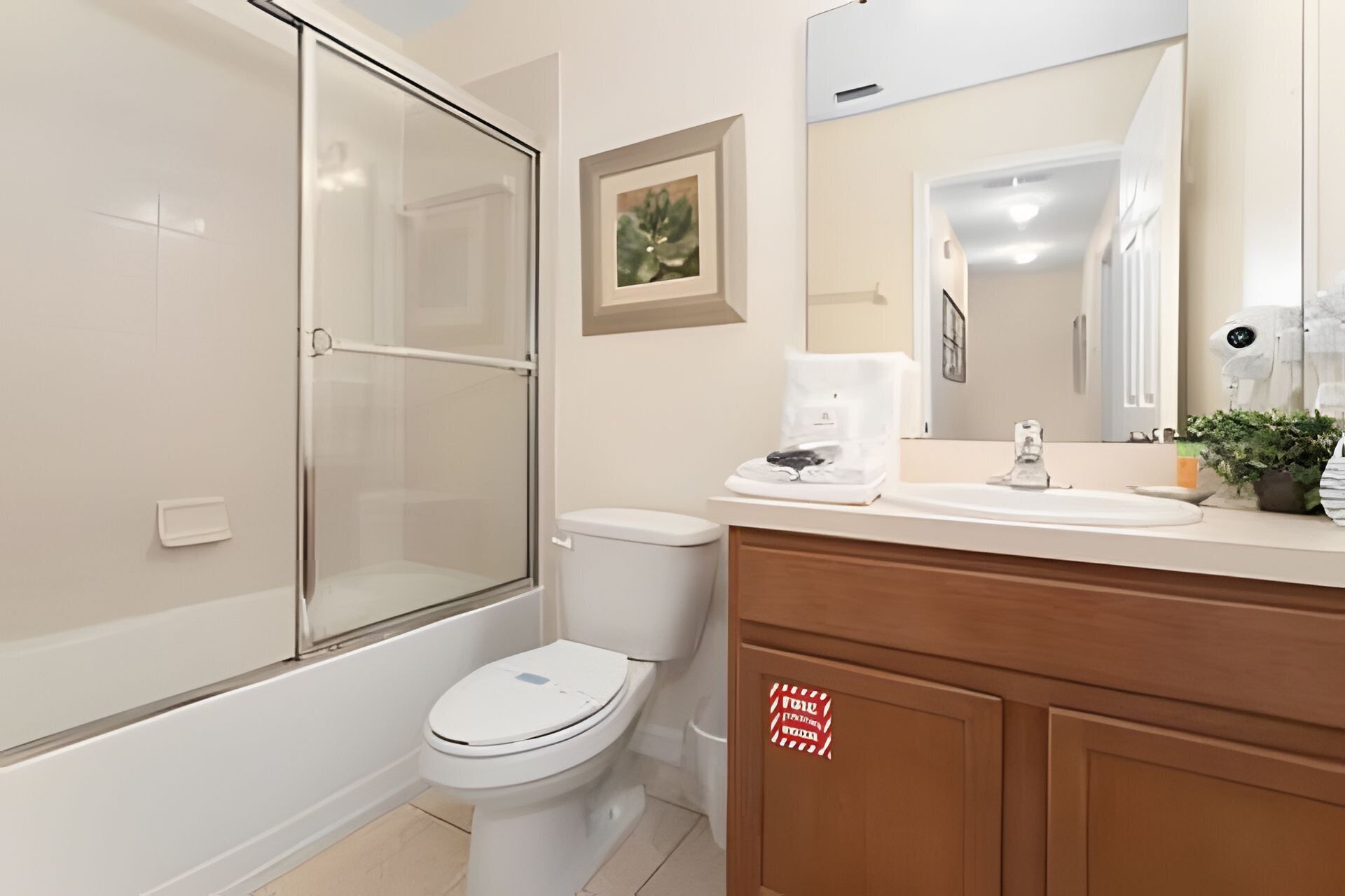 A modern bathroom with a glass-enclosed shower, a toilet, a sink with a coffee maker, and a wooden vanity.