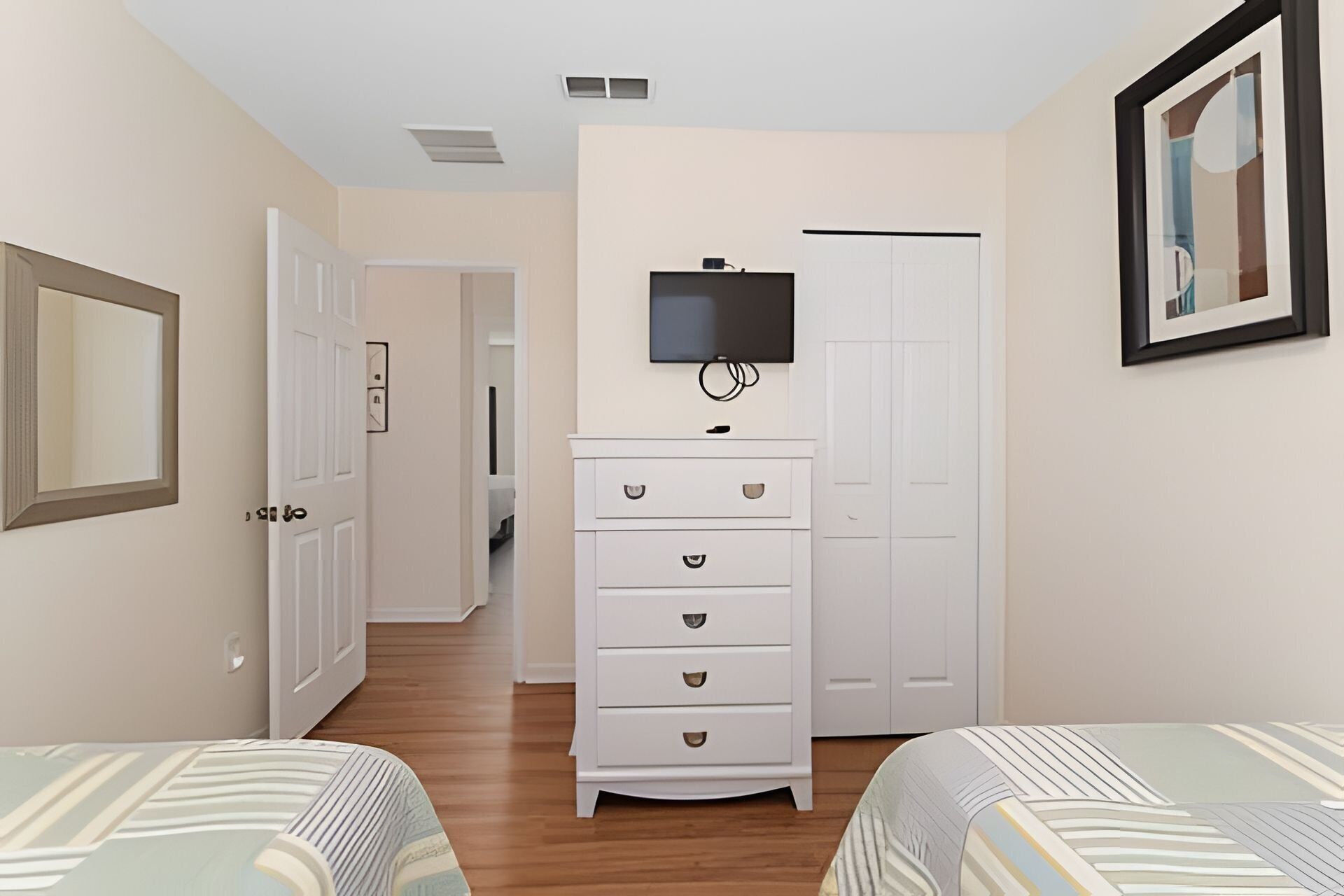 Une chambre avec deux lits, une commode, un téléviseur et un tableau encadré au mur.