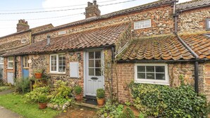 Une maison traditionnelle en pierre, avec un toit en tuiles, une porte d’entrée et un petit jardin agrémenté de plantes en pot.
