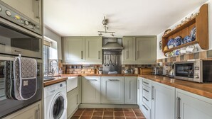 Une cuisine équipée d’un lave-linge, d’un four, d’un four à micro-ondes et d’une étagère où sont rangés la vaisselle.