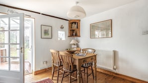 Un coin repas comprenant une table en bois, quatre chaises, une lampe et une étagère ornée d’objets décoratifs.