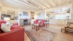 Sala de estar con un sofá rojo, una mesa de centro y un tapete estampado. Cuenta con una chimenea, una cocina al fondo y un comedor con una silla de madera.