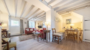 Un salón amplio con un sofá rojo, sillas de madera, una mesa de comedor y una zona de cocina con refrigerador.