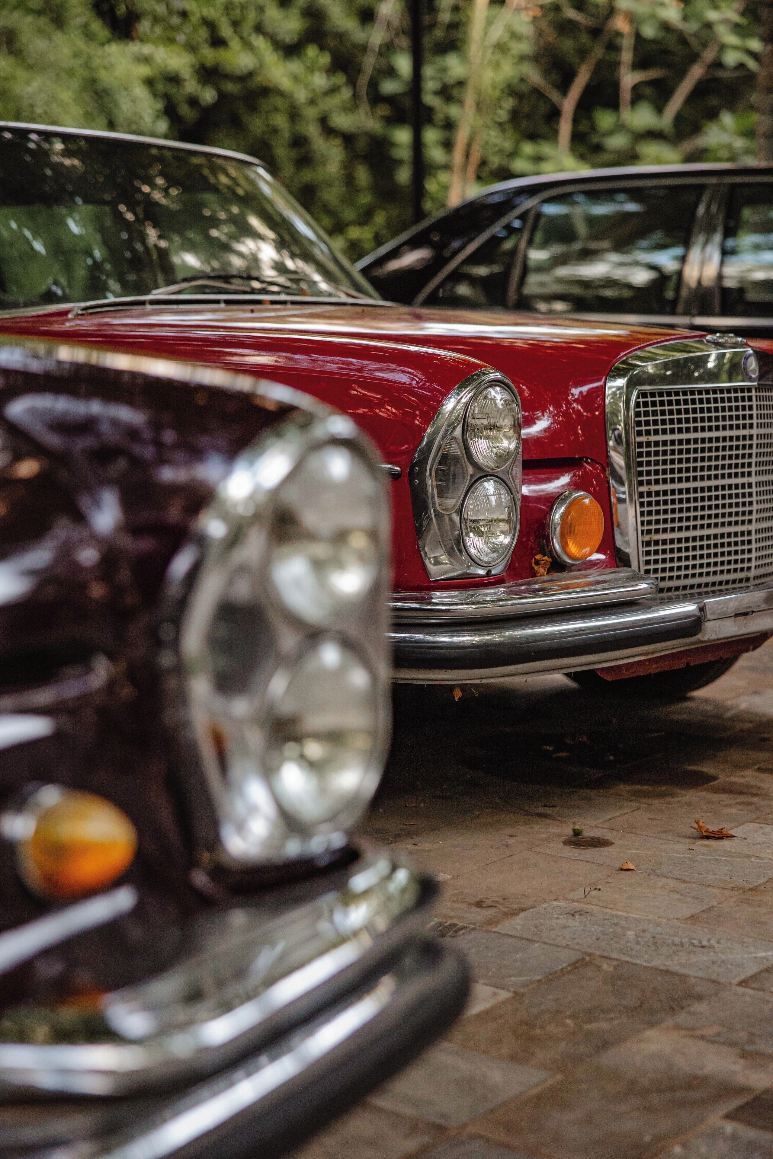 Une voiture rouge ancienne est garée sur une surface pavée, avec un arrière-plan flou de verdure.