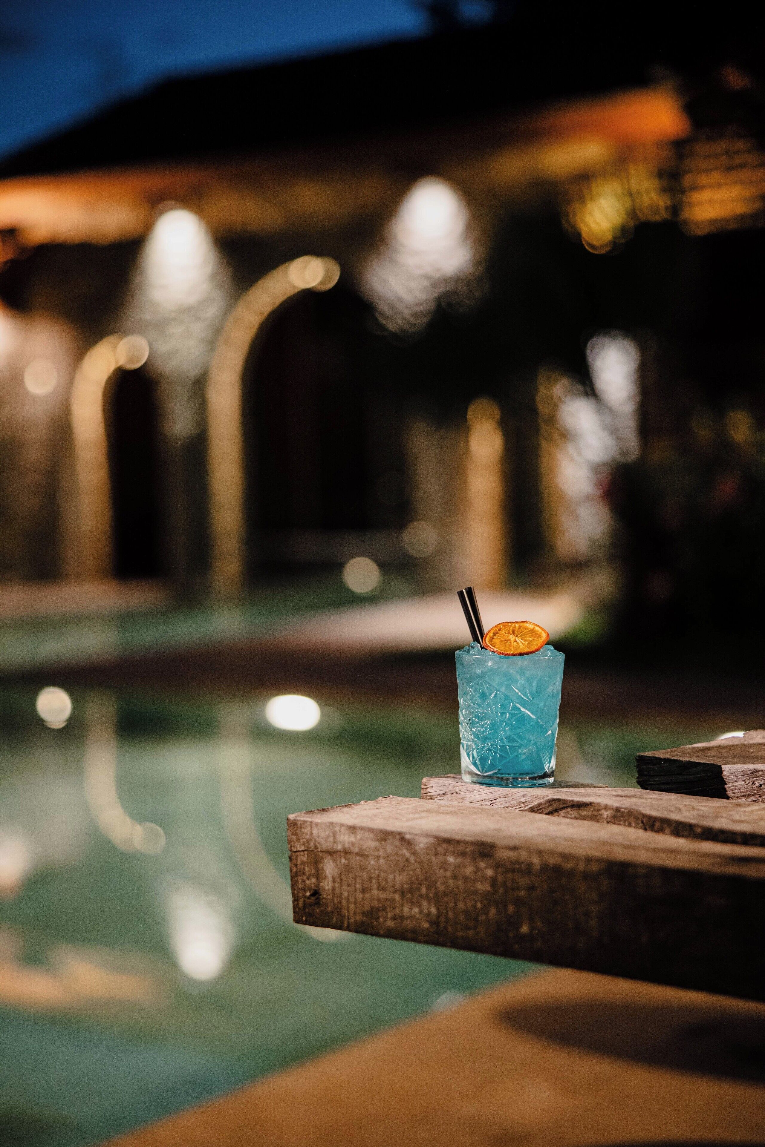 A clear view of a poolside bar with a drink and a wooden table.