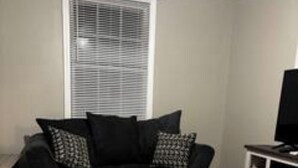 Een woonkamer met een zwarte bank, een salontafel en een televisietoestel op een dressoir.