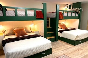 Ein Zimmer mit zwei Etagenbetten, jeweils mit Kopfkissen und Decke. Zwei Nachttische mit Lampen und ein kleines Regal mit einem dekorativen Gegenstand.