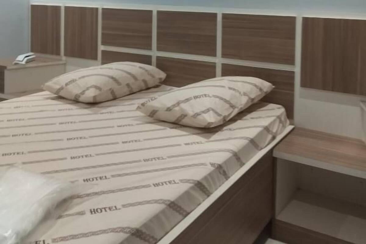Habitación de hotel con una cama, dos almohadas, una mesita de noche, un teléfono y un equipo de aire acondicionado.