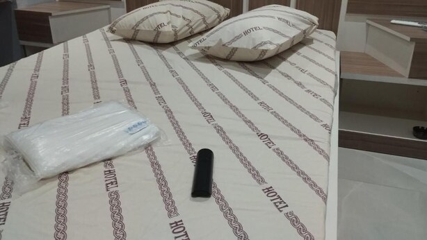 Una cama con una colcha a rayas, dos almohadas y un objeto negro sobre la cama.