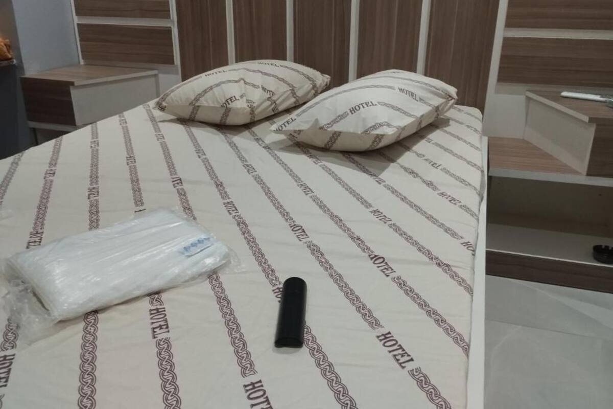 Una cama con una colcha a rayas, dos almohadas y un objeto negro sobre la cama.