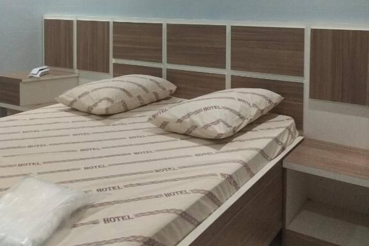 Habitación de hotel con cama, dos almohadas, mesita de noche, lámpara y equipo de aire acondicionado.